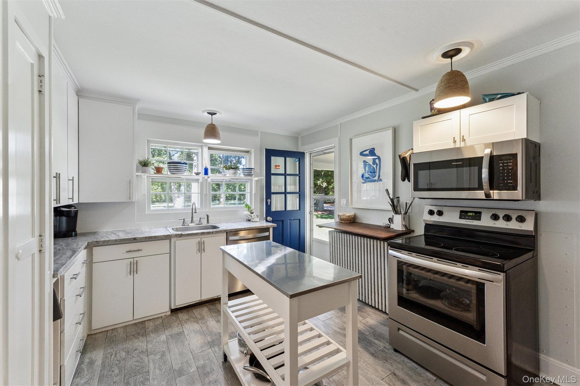 Kitchen featuring stainless steel appliances, crown molding, hanging light fixtures, white cabinetry, and light wood finished floors