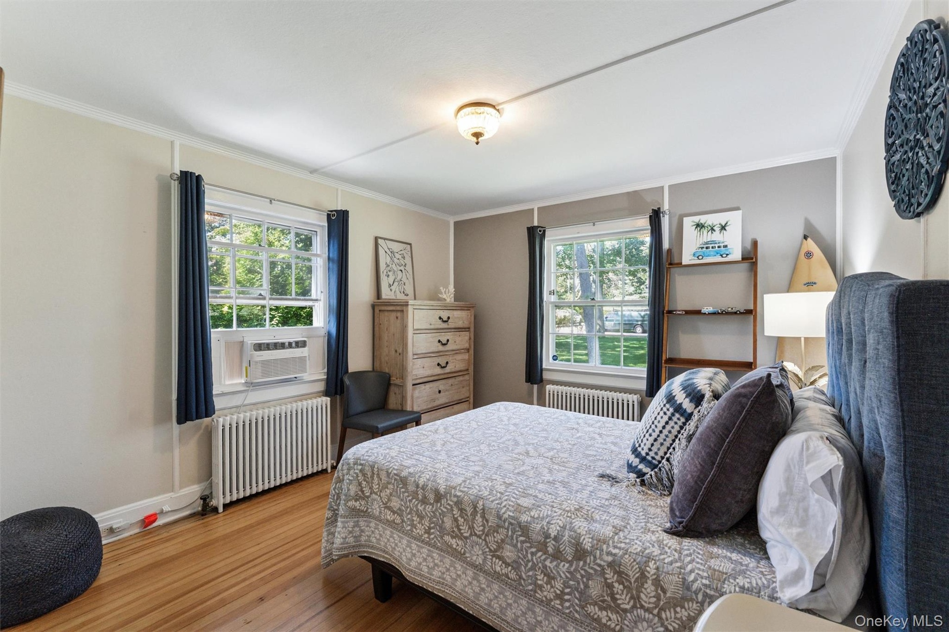 Bedroom with radiator, multiple windows, wood finished floors, and ornamental molding
