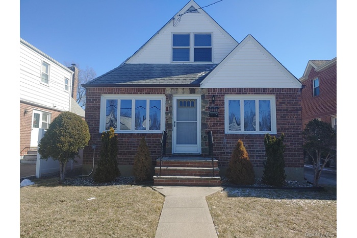 Bungalow-style home featuring entry steps, a shingled roof, a front lawn, and brick siding