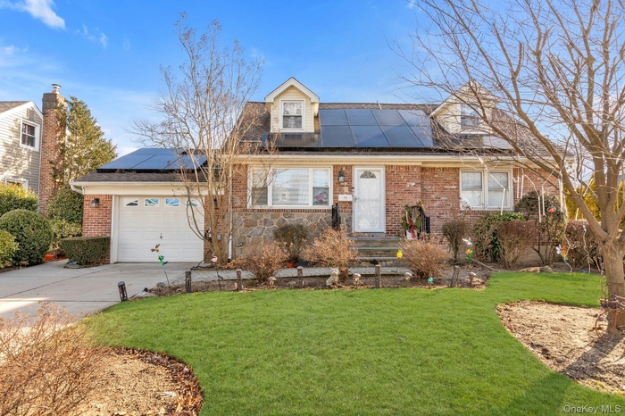 Cape cod house with a front yard, roof mounted solar panels, concrete driveway, and brick siding