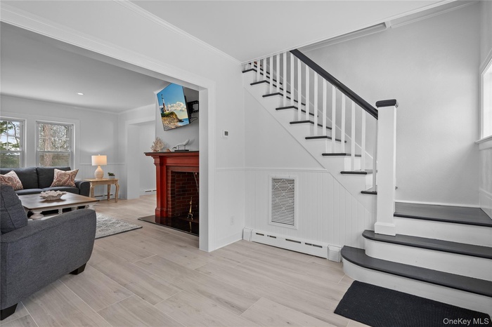 Staircase with healthy amount of natural light, a baseboard heating unit, wainscoting, a fireplace with raised hearth, and crown molding