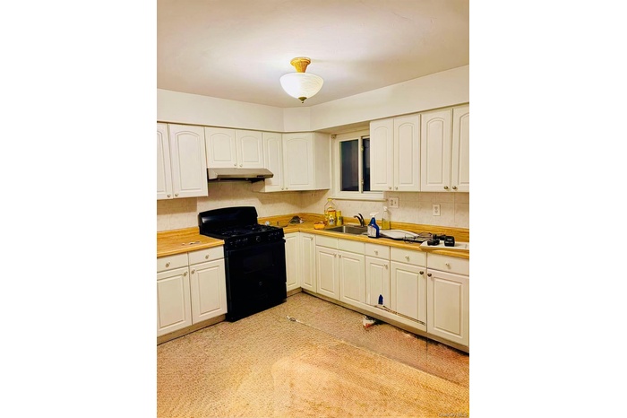 Kitchen featuring black gas range oven, light countertops, white cabinets, and under cabinet range hood