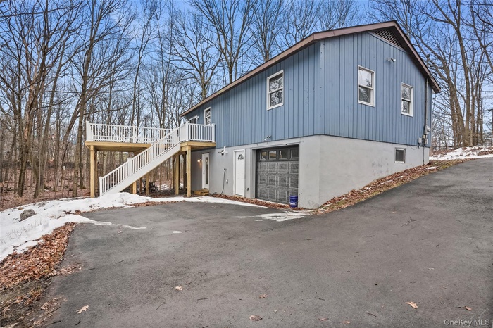 View of side of property featuring a deck, a garage, stairs, and asphalt driveway