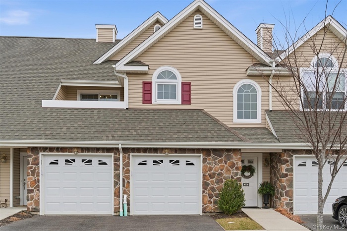 View of front of house featuring stone siding, a chimney, asphalt driveway, a shingled roof, and an attached garage