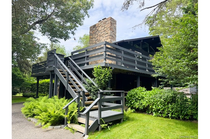 Rear view of property featuring a wooden deck, stairs, a chimney, and a yard