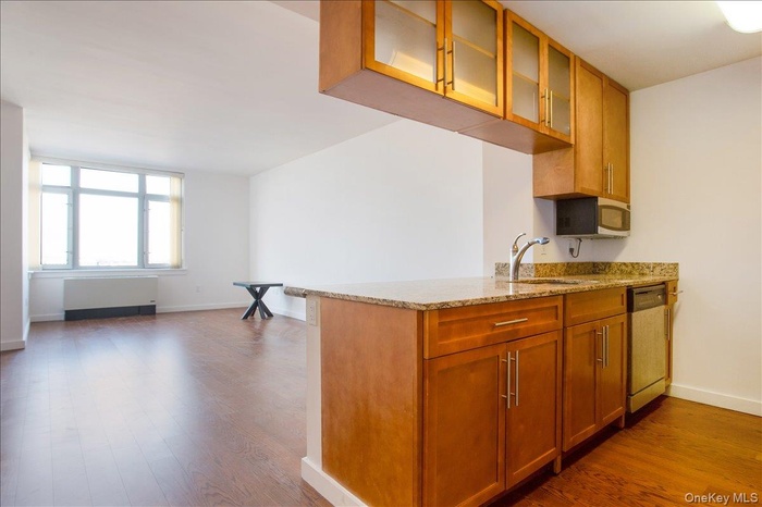 Kitchen with brown cabinetry, light stone counters, glass insert cabinets, a peninsula, and stainless steel appliances