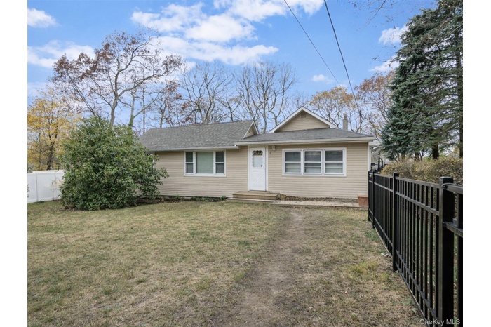 Single-story home featuring neutral siding, a welcoming front entry, and a spacious front yard with mature trees, fencing, and a private, residential 