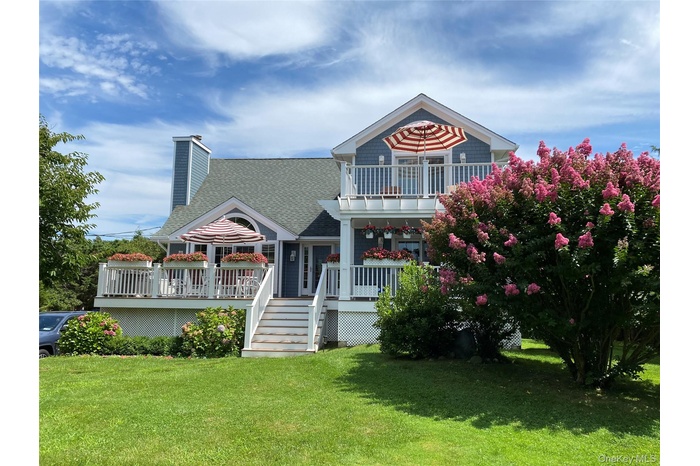 View of front of property with a shingled roof, a front lawn, a chimney, stairway, and covered porch