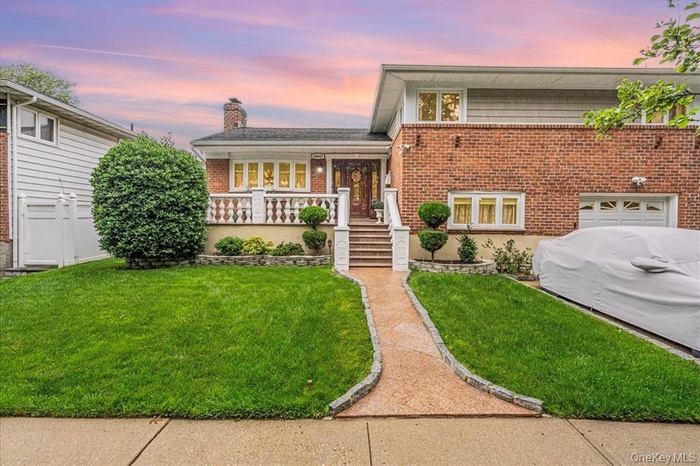 Split level home with a porch, a front yard, a chimney, brick siding, and a garage