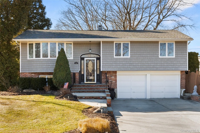 Raised ranch featuring concrete driveway, a chimney, a garage, and brick siding