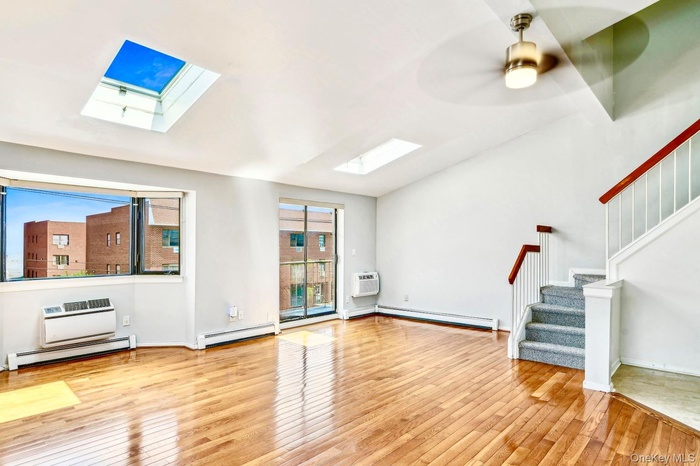 Unfurnished living room featuring healthy amount of natural light, a skylight, a baseboard radiator, and light wood-style floors