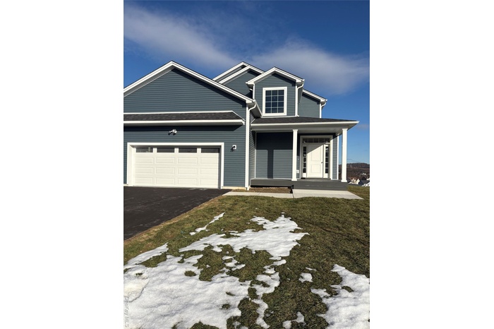 View of front of home with driveway, covered porch, an attached garage, and a front lawn