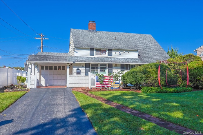 Traditional-style home with a shingled roof, a chimney, an attached garage, driveway, and a porch