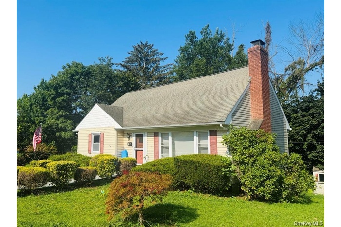 Cape cod-style house featuring a chimney, a front yard, and roof with shingles