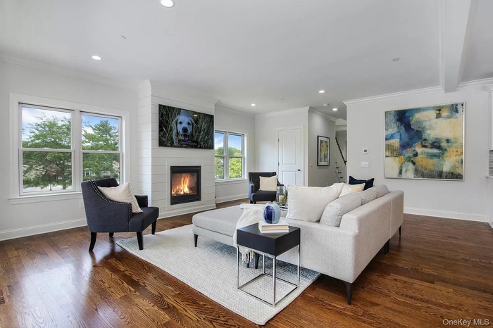 Living area with dark wood-style flooring, a large fireplace, ornamental molding, and recessed lighting