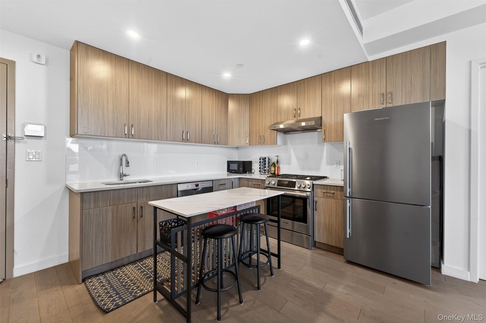 Kitchen featuring appliances with stainless steel finishes, light wood-type flooring, under cabinet range hood, light stone counters, and recessed lig