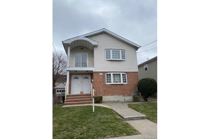 View of front of home featuring a balcony, brick siding, and a front yard