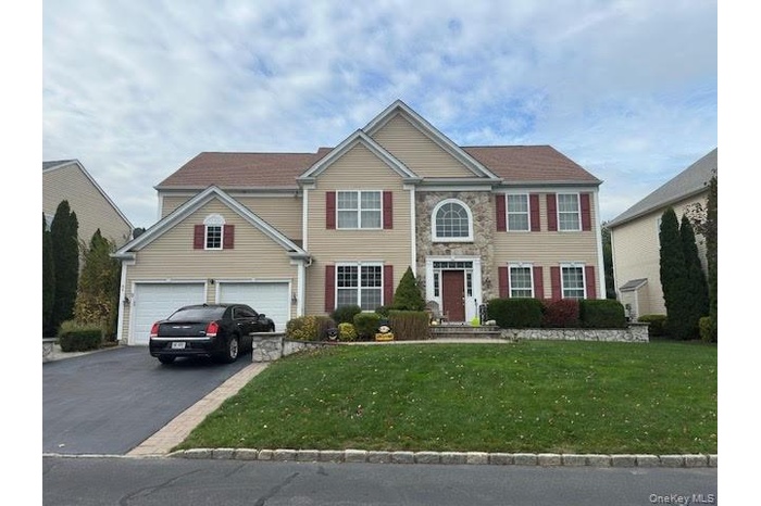 View of front of home featuring asphalt driveway, a front yard, an attached garage, and stone siding