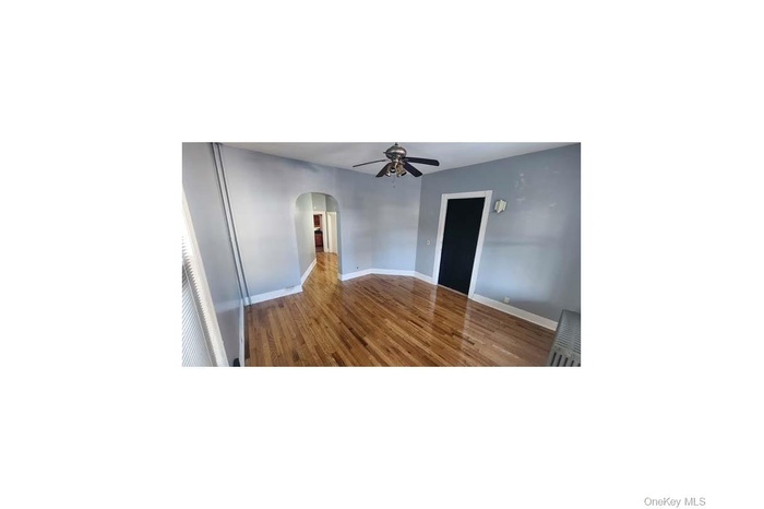 Spare room with arched walkways, dark wood-type flooring, and a ceiling fan