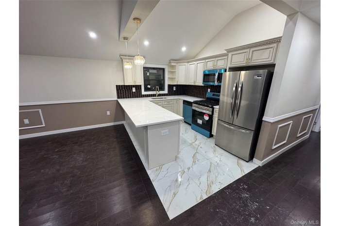 Kitchen with stainless steel appliances, hanging light fixtures, a peninsula, vaulted ceiling, and light marble finish flooring