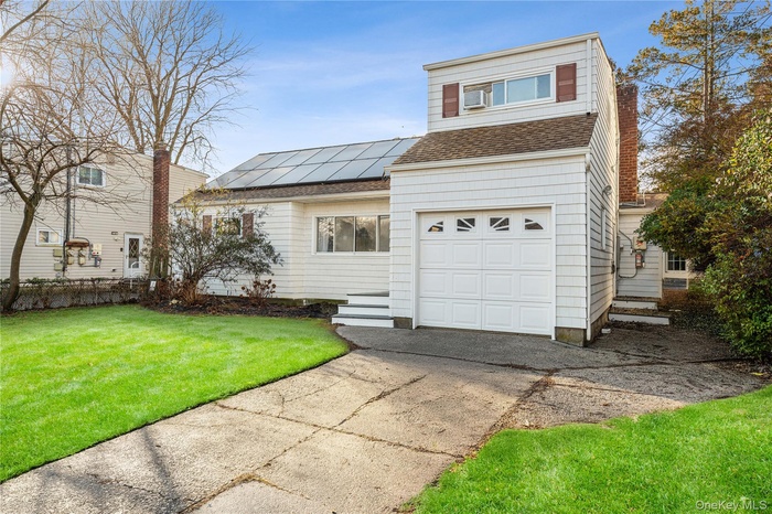 View of front facade featuring a shingled roof, a front yard, solar panels, a garage, and concrete driveway