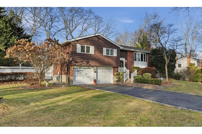 Bi-level home featuring a chimney, a front lawn, driveway, and an attached garage