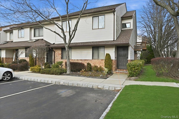 View of front facade with uncovered parking, brick siding, a shingled roof, and a front lawn