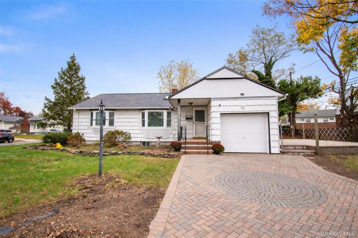 View of front of house featuring decorative driveway, a chimney, a front yard, and a garage
