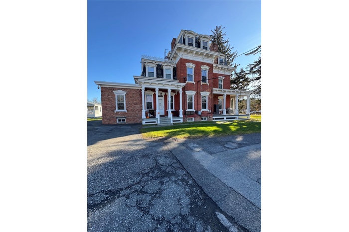 Second empire-style home with mansard roof, brick siding, covered porch, and a high end roof