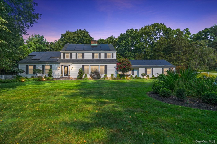 Front of home with lighted walkway featuring roof mounted solar panels and a lawn