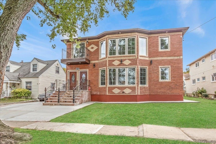 View of front facade with brick siding, a balcony, and a front lawn