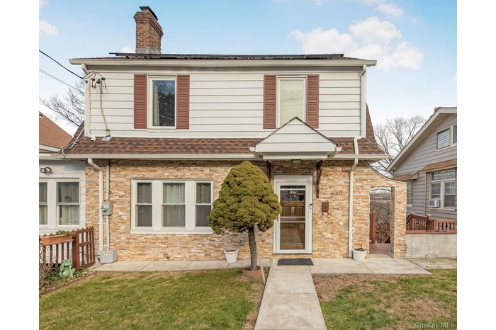 View of front of home with a front lawn, a chimney, a patio area, and stone siding