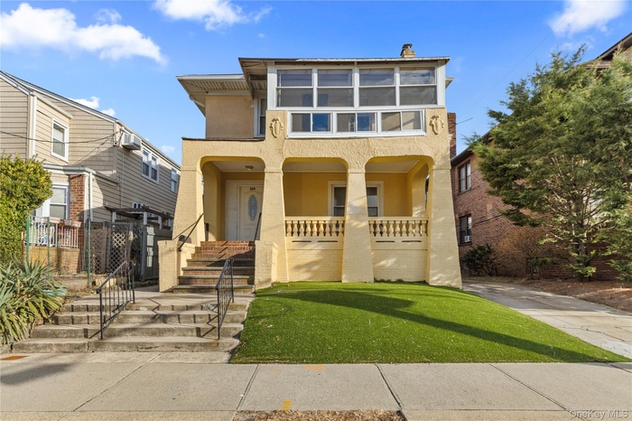 View of front facade featuring stucco siding, covered porch, a chimney, and a front yard