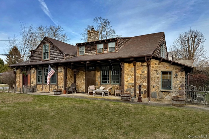 Back of property with stone siding, a chimney, roof with shingles, and a patio