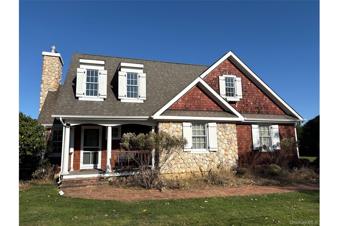 View of front of home with a chimney, a front porch, stone siding, a front lawn, and a shingled roof