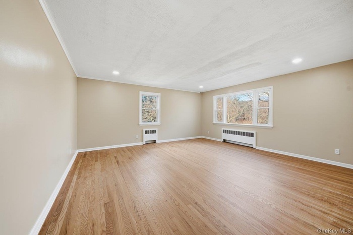 Unfurnished room with radiator, light wood-style floors, and recessed lighting