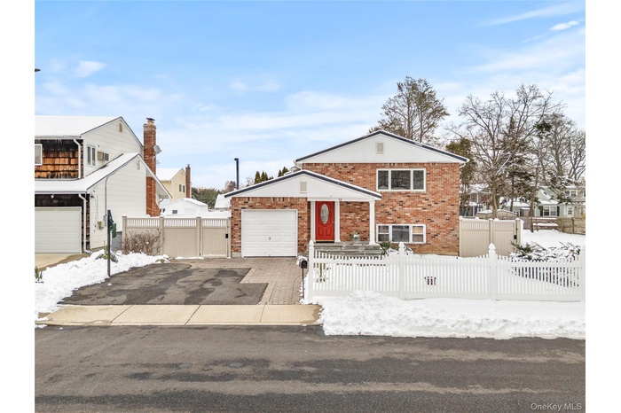 Tri-level home featuring brick siding, driveway, a fenced front yard, and an attached garage
