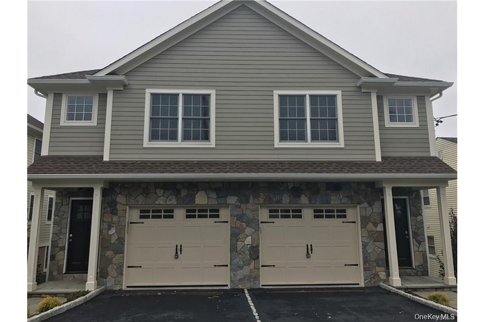 View of front of house with stone siding, driveway, and roof with shingles