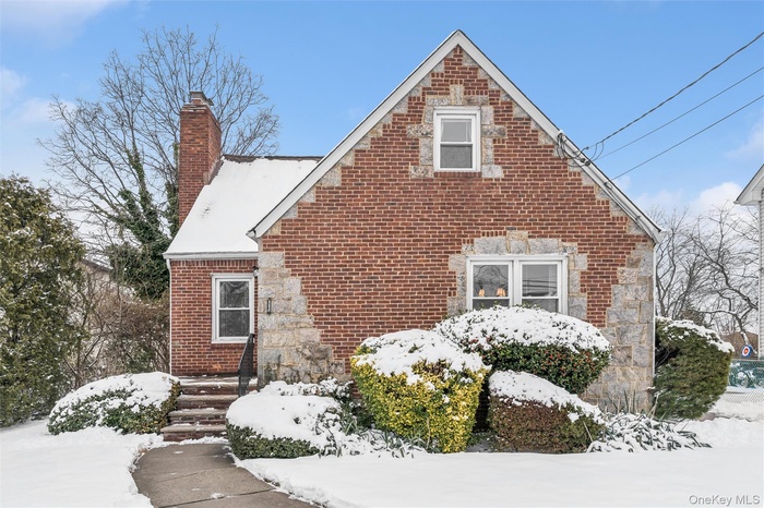 View of snow covered exterior featuring brick siding and a chimney