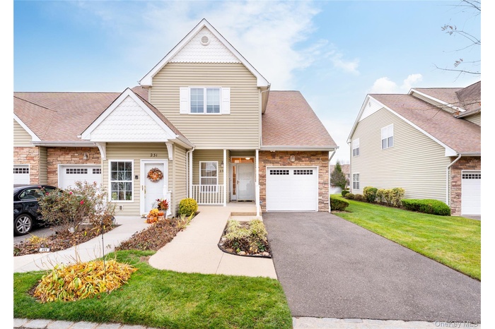 View of front facade with stone siding, roof with shingles, an attached garage, asphalt driveway, and a front yard