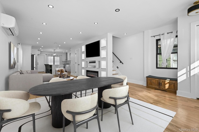 Dining area featuring recessed lighting, a glass covered fireplace, a wall mounted air conditioner, stairway, and light wood-style flooring