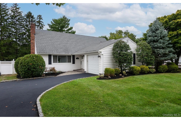 View of front of house with an attached garage, driveway, roof with shingles, and a chimney