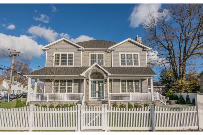 View of side of the home with wrap around porch, a shingled roof and fenced in property. out door lighting.