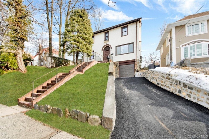 View of front facade with stucco siding, stone siding, a front yard, stairway, and an attached garage