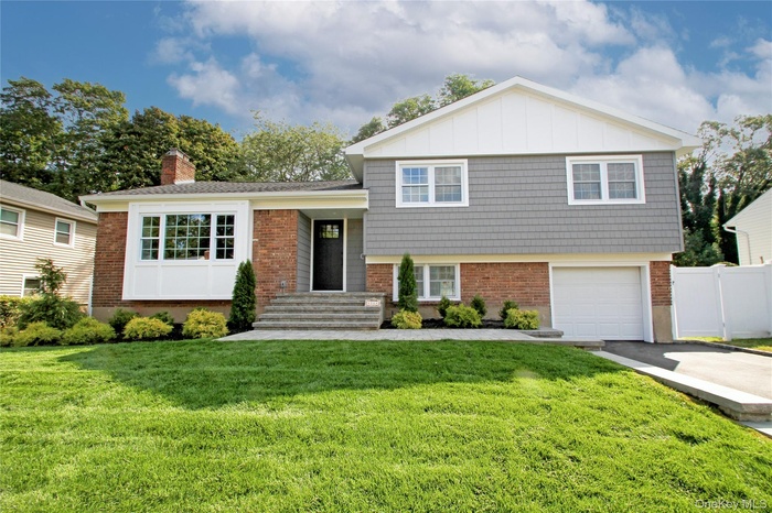 Tri-level home featuring asphalt driveway, brick siding, a garage, a chimney, and board and batten siding