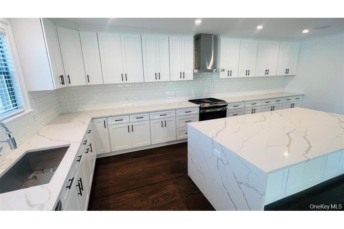 Kitchen with a kitchen island, white cabinetry, light stone countertops, wall chimney range hood, and stainless steel gas range oven