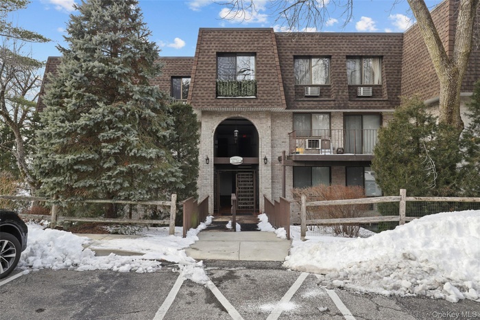 View of front of home featuring mansard roof, brick siding, a shingled roof, a fenced front yard, and uncovered parking