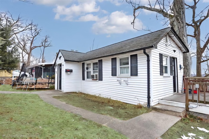 View of side of home with roof with shingles, a wooden deck, and a yard