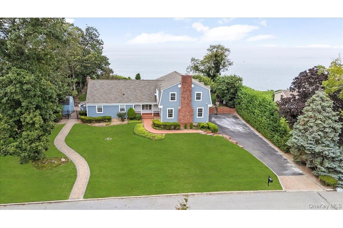 View of front of home with a front lawn, driveway, a chimney, and a water view