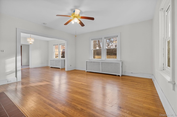 Unfurnished room featuring radiator heating unit, a chandelier, light wood-style flooring, a ceiling fan, and healthy amount of natural light